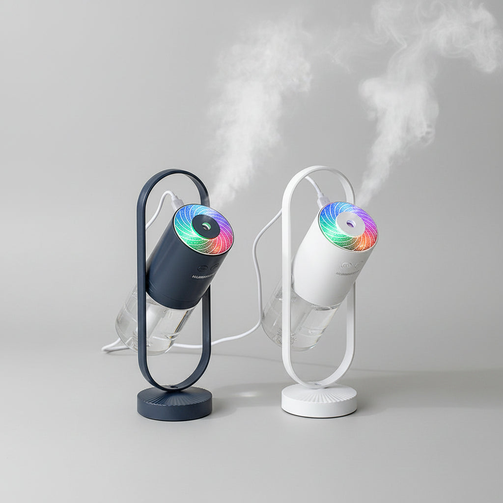 Two portable mist humidifiers with cylindrical water tanks and illuminated rainbow LED tops, shown in a styled indoor setting with visible mist and a glass vase in the background.